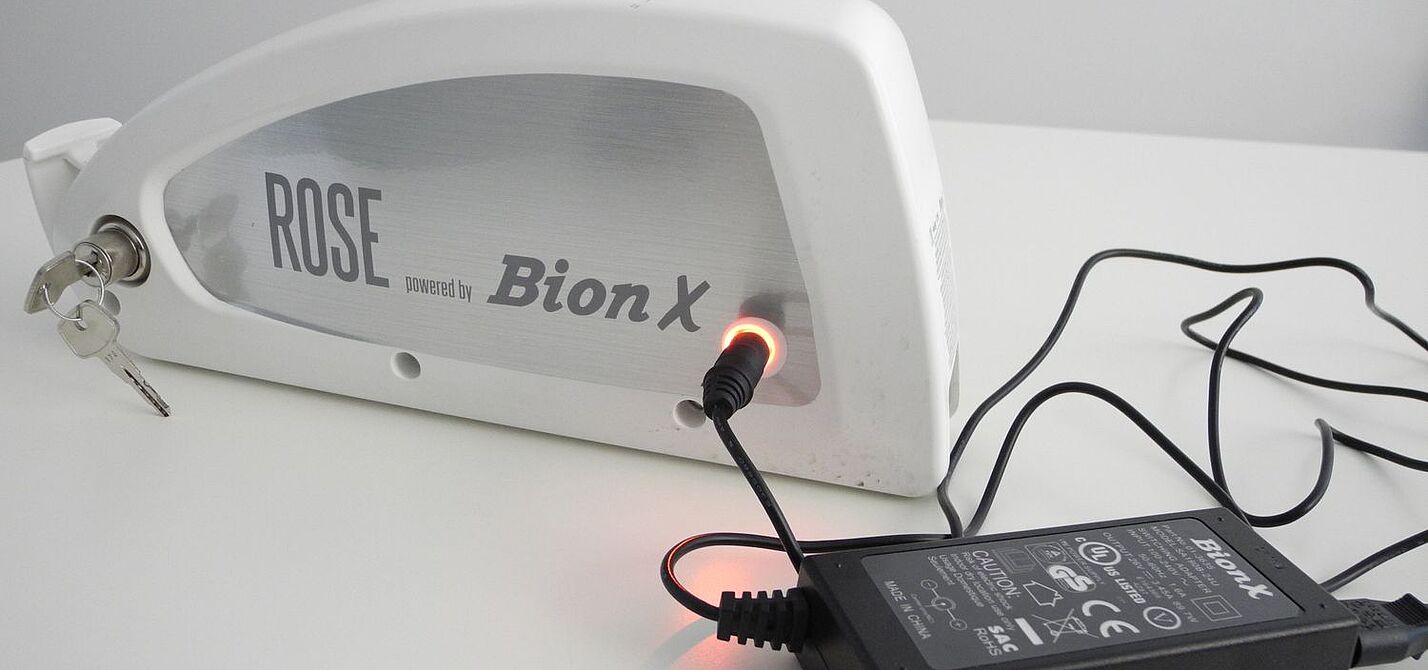 Ein Elektrorad-Akku steht auf einem Tisch und ist am Netzteil angeschlossen. 