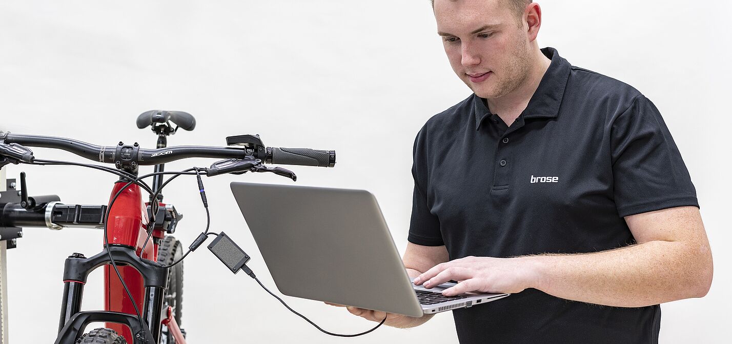 Die Motorsteuerung eines Elektrofahrrads wird von Fachleuten ausgelesen. Auch illegales Tuning lässt sich so nachweisen. Mann mit Laptop steht neben einem Fahrrad. Das Laptop ist an das Fahrrad angeschlossen. Der Mann liest die elektronisch verfügbaren Daten mit seinem Laptop vom Fahrradmotor aus.